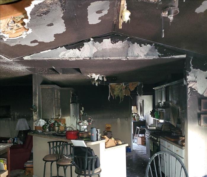 A fire-damaged kitchen with damaged walls, ceilings, and soot-covered furnishings