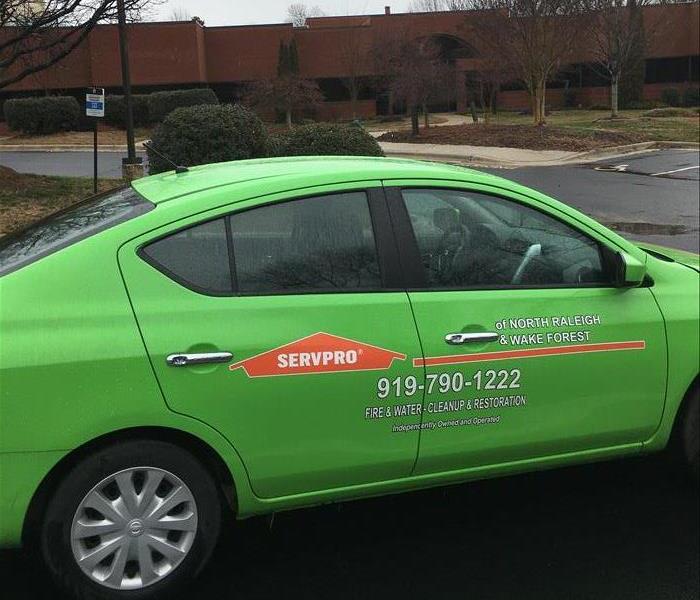 green SERVPRO car sitting in front of a red brick building